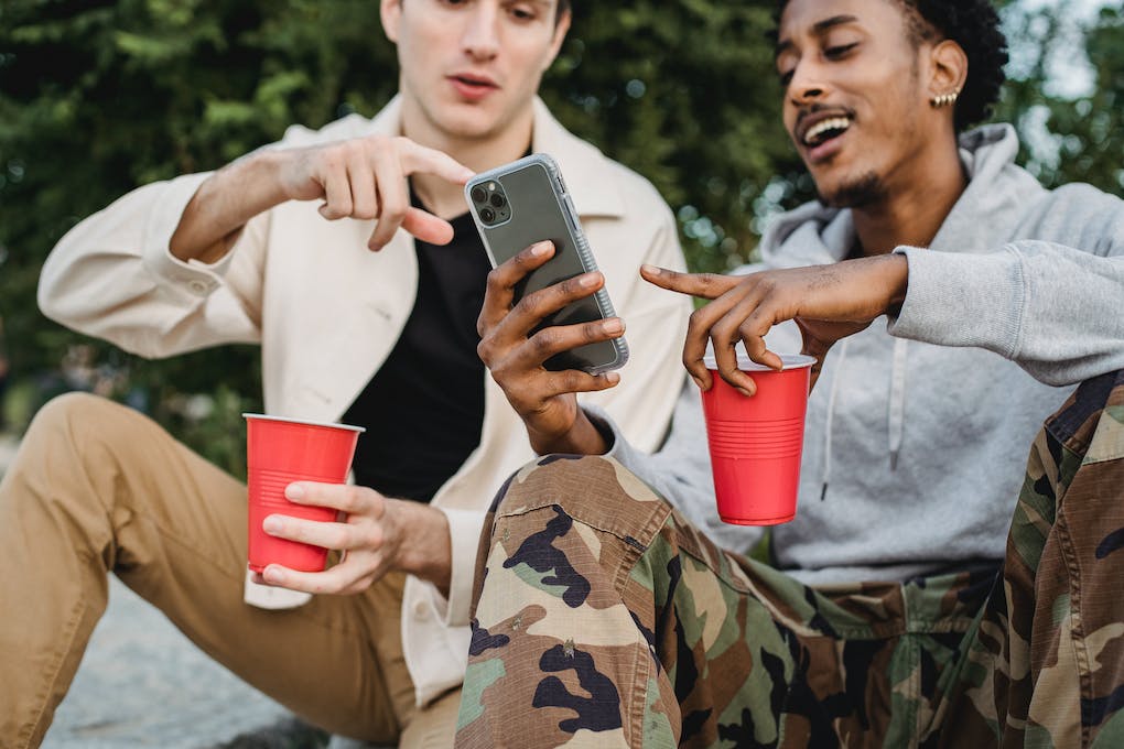 Two friends sit outdoors, looking at a phone and holding red cups, perhaps discussing their favorite loyalty program.