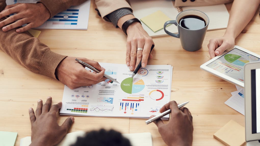 A group of people reviewing charts and graphs on paper, with a cup of coffee and tablet on the table, discuss insights from the new loyalty program.