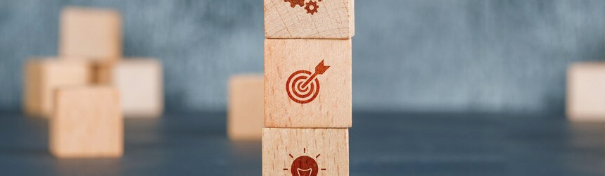 Three stacked wooden blocks with icons of a cogwheel, a target, and a lightbulb, representing ideas, goals, and the essence of a loyalty program.