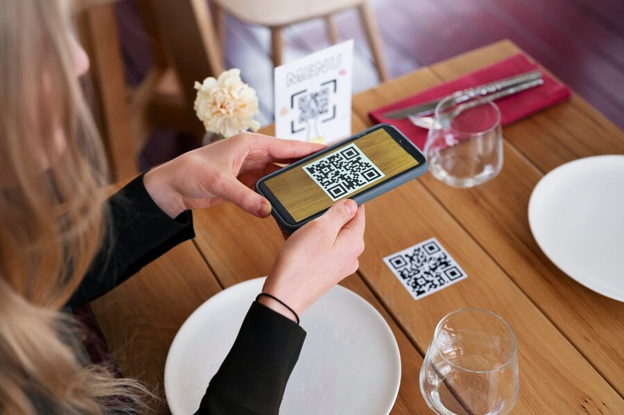 A person is scanning a QR code on the table with a smartphone in a restaurant, seamlessly linking it to their digital loyalty card for rewards.