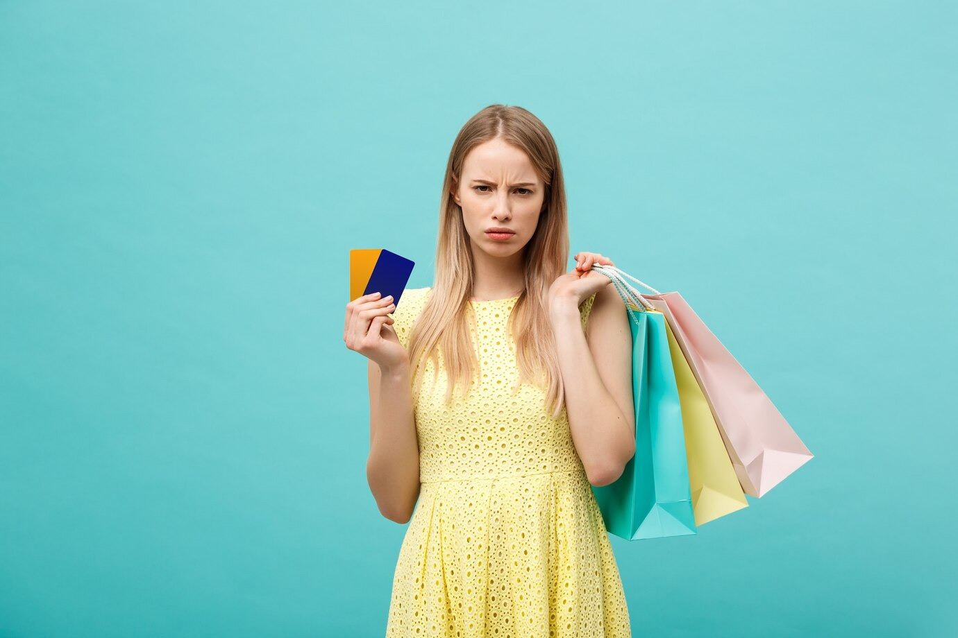 A woman in a yellow dress looks concerned while holding shopping bags, credit cards, and a loyalty card against a teal background.