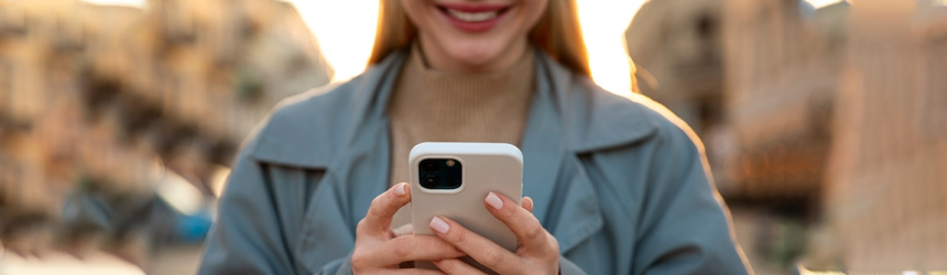 A smiling person holds a smartphone displaying a Digital Loyalty Card while standing outdoors in a bustling city setting.